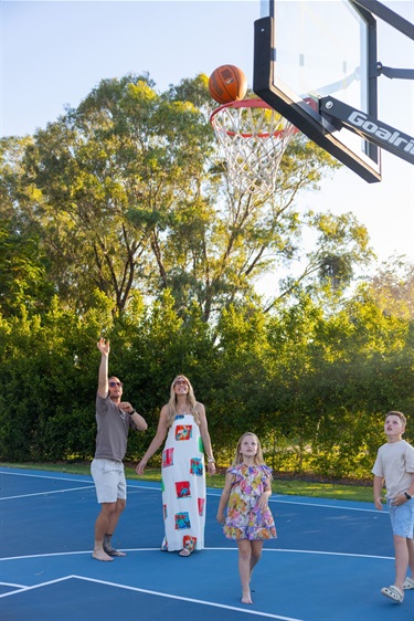 A man throws a basketball towards a hoop on a small court while his family watch