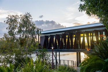 A modern metallic restaurant surrounded by trees and overlooking a river