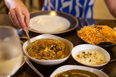 A woman stirs a bowl of curry on a restaurant table surrounded by other dishes