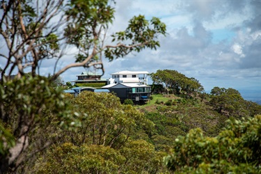 Large modern houses are perched on top of a hill, surrounded by vegetation and looking over a valley