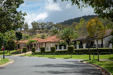 Large modern homes sit in a residential street backing onto hills, with green nature strips and sculpted trees out the front