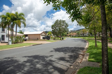 Large modern homes sit in a tree-lined residential street backing onto hills