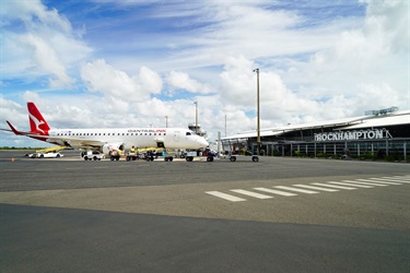 Luggage is being loaded onto a airport baggage vehicle from a QantasLink jet parked on the tarmac outside the Rockhampton Airport terminal.