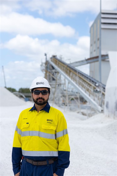 A man wearing high visibility clothes and a hard hat looks at the camera amongst piles of white rocks