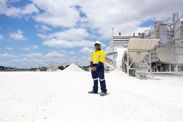 A man wearing high visibility clothes and a hard hat looks off into the distance amongst piles of white rocks