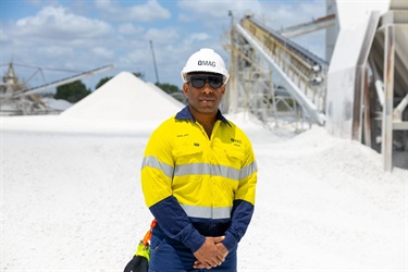 A man wearing high visibility clothes and a hard hat looks at the camera amongst piles of white rocks