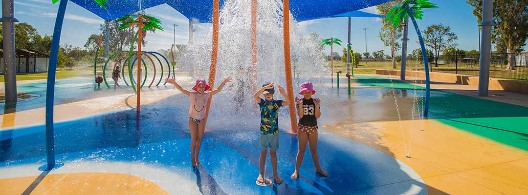 Three children stand in a water park with water pouring onto them from above