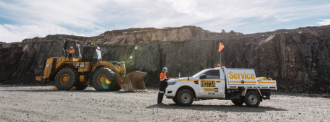 An excavator and mine-spec ute are parked in front of an excavated mine wall