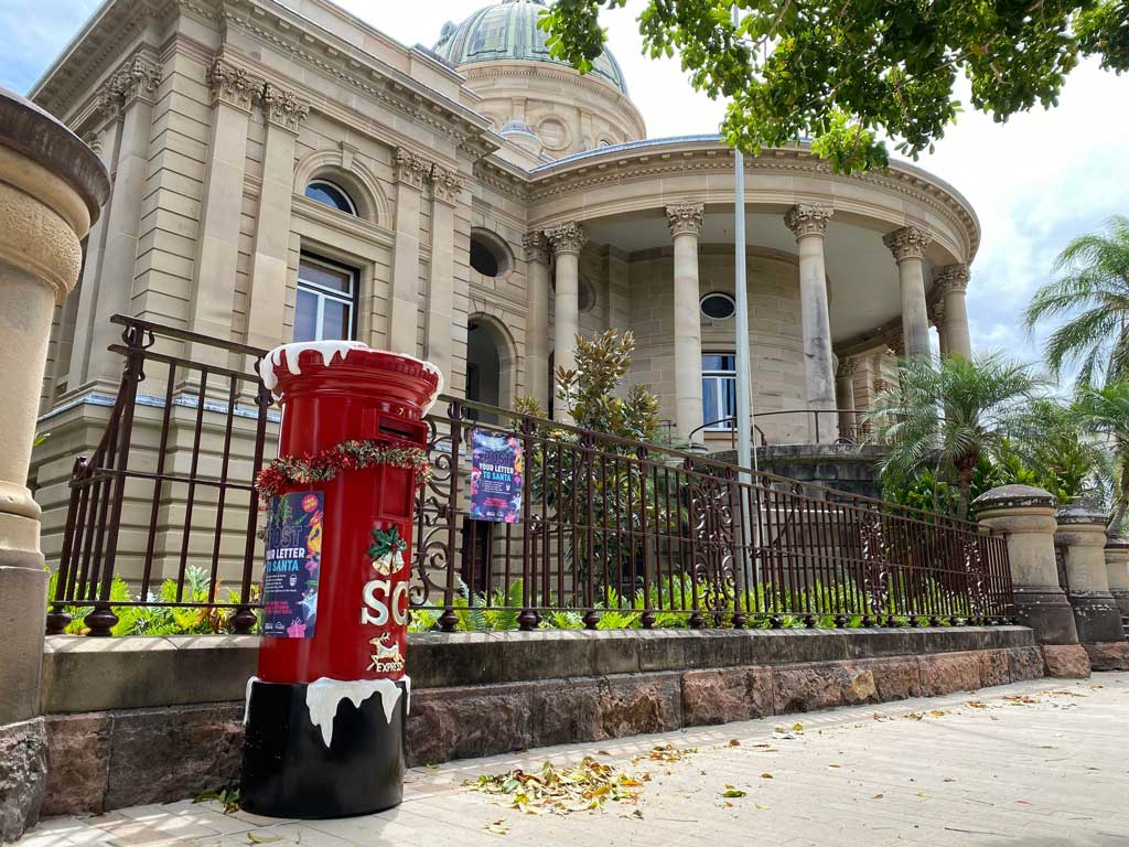 A snow covered, red postbox stands in front of Rockhampton's Customs House