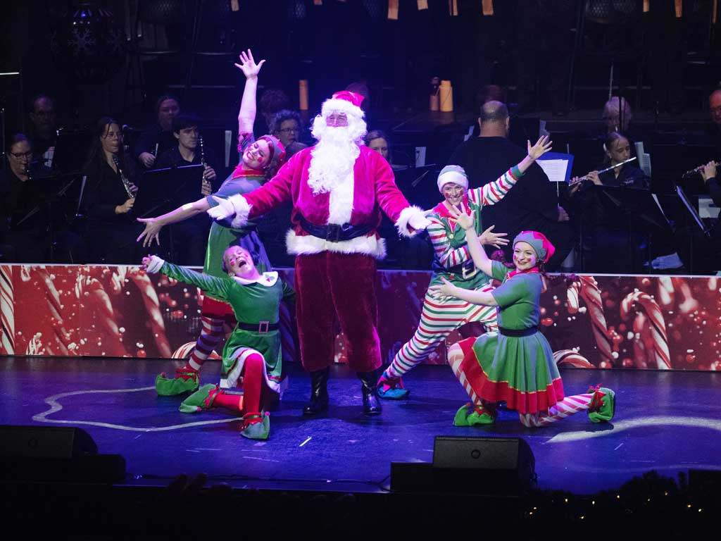 Santa and four elves perform on stage at a Carols by Candlelight event