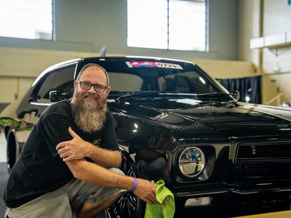 A man kneels in front of his prized classic car