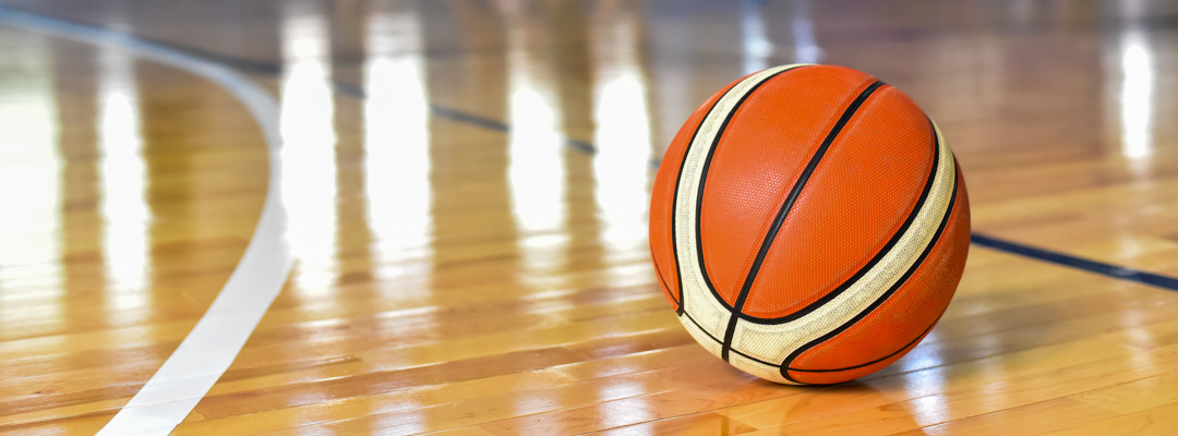 A basketball sits on the floor of an indoor basketball court