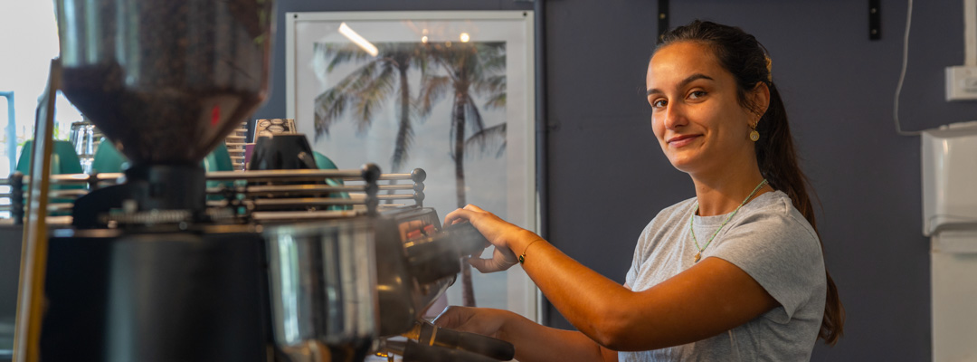 A woman smiles at the camera as she operates a coffee machine
