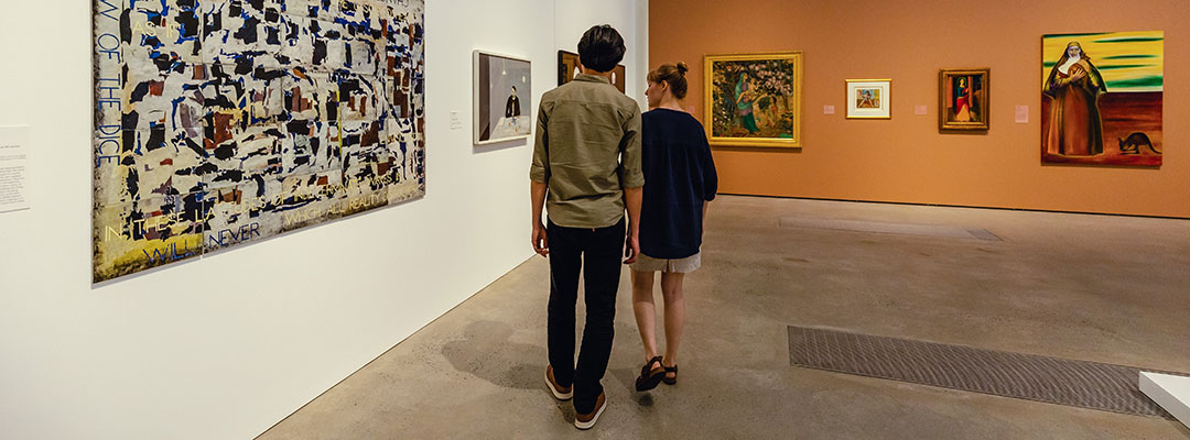 A couple walks past paintings inside RMOA