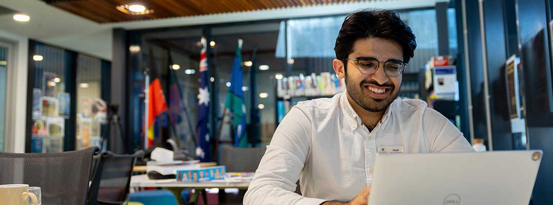 A university student smiles as he uses a laptop inside a modern study area