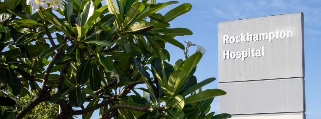 Green trees in front of a grey sign reading 'Rockhampton Hospital'