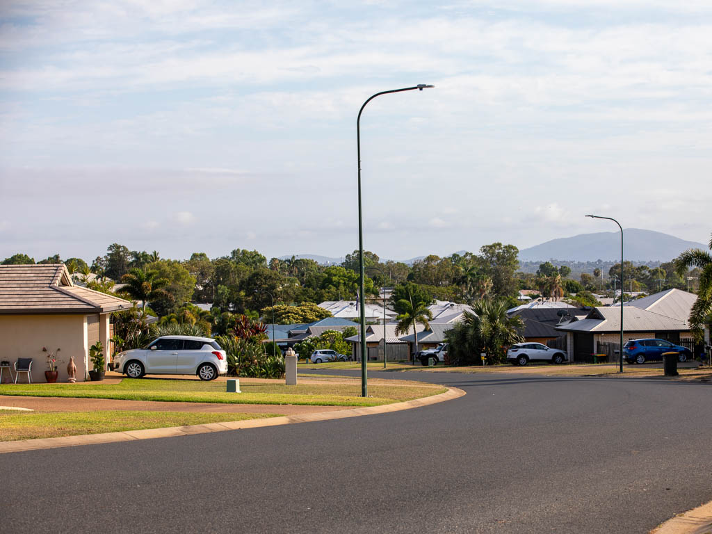 Rows of modern houses recede along a tidy street, with trees and mountains in the distance