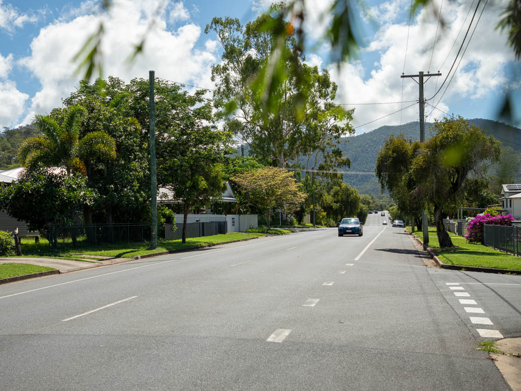 A tree-lined residential street recedes into the distance towards a green mountain