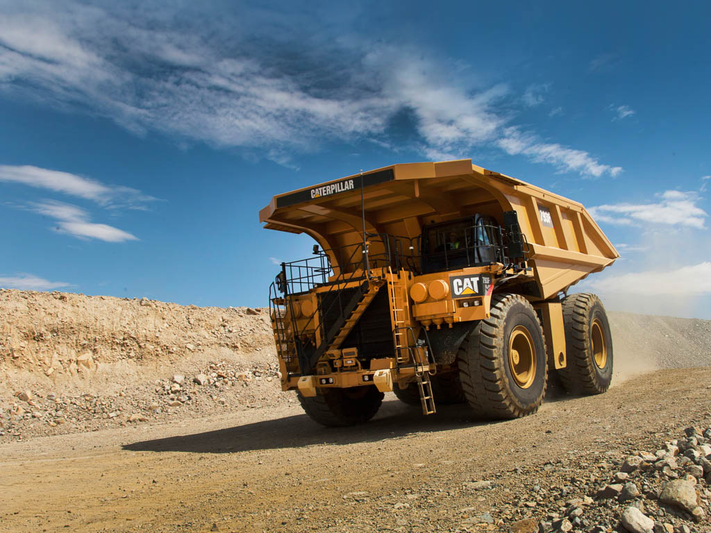 A large dump truck driving down a dirt road at at a mine site, with a pile of rocks in the background