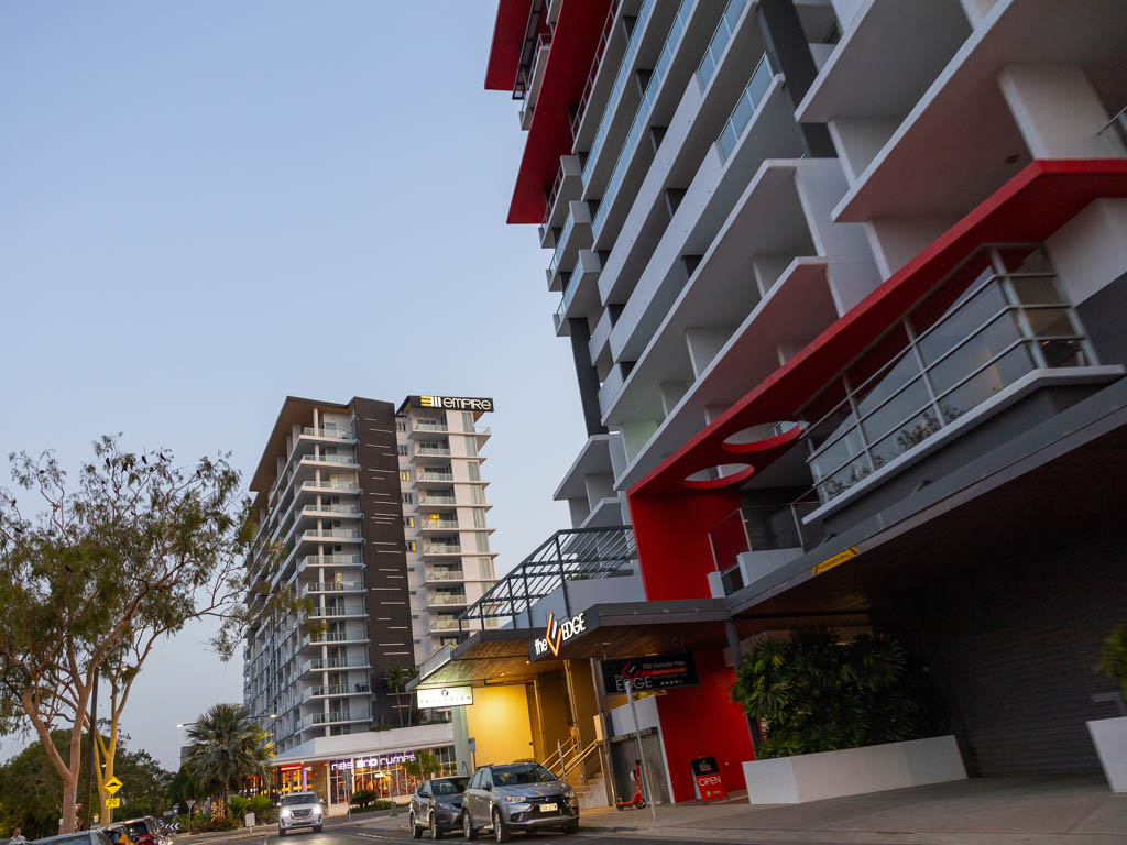 Two high-rise apartment buildings branded 'Empire' and 'The Edge' dominate over a city street, where cars are parked as the sun sets